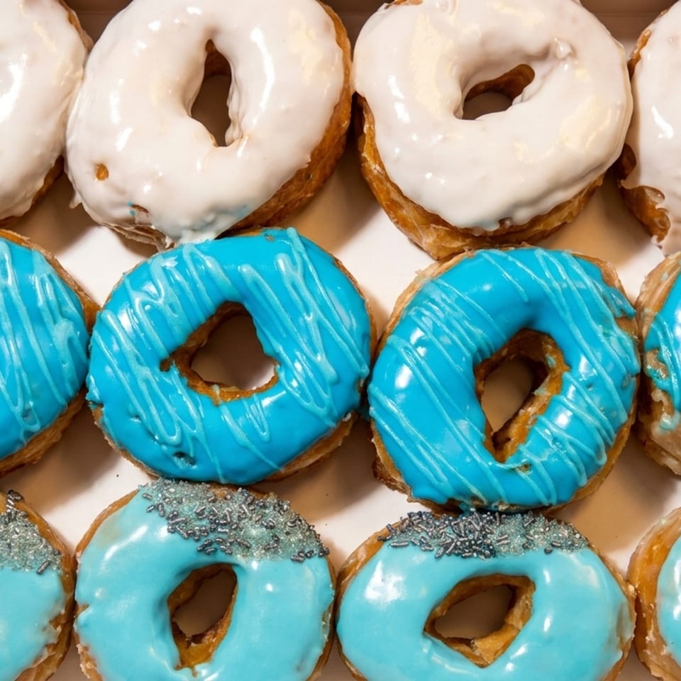 A box of twelve donuts, four white frosted, four blue frosted, and four light blue with sprinkles.