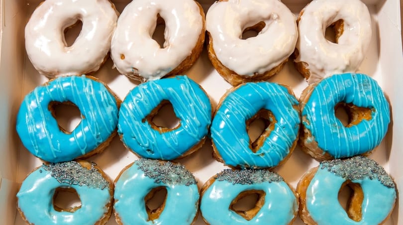 A box of twelve donuts, four white frosted, four blue frosted, and four light blue with sprinkles.