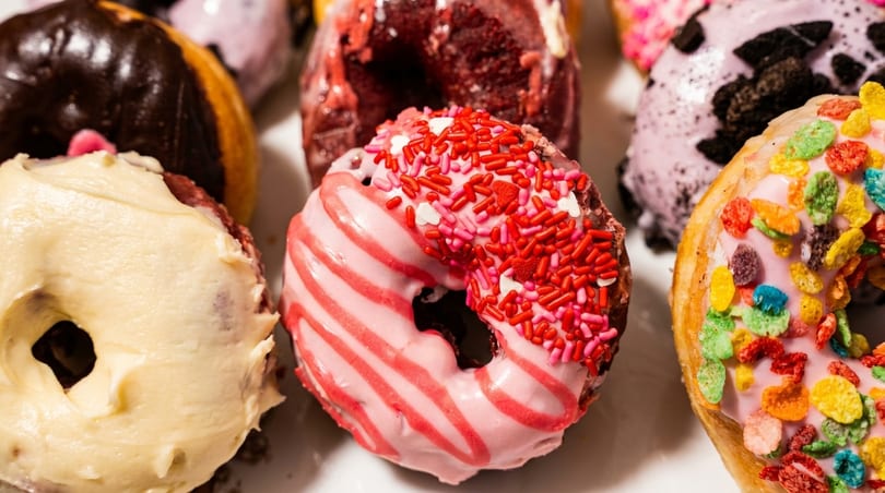 Close-up of assorted colorful donuts with various frostings and sprinkles, including pink, chocolate, and cereal.