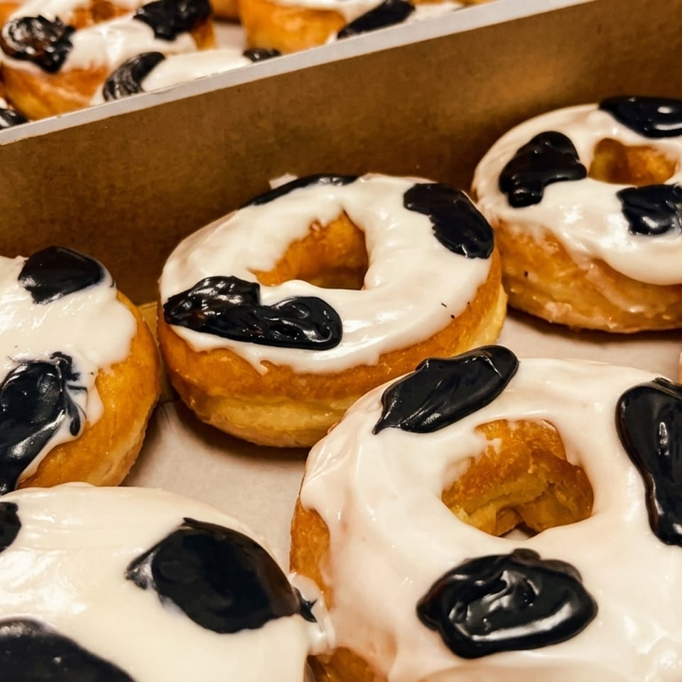 A box filled with many cow-print donuts, featuring white glaze with black splotches.