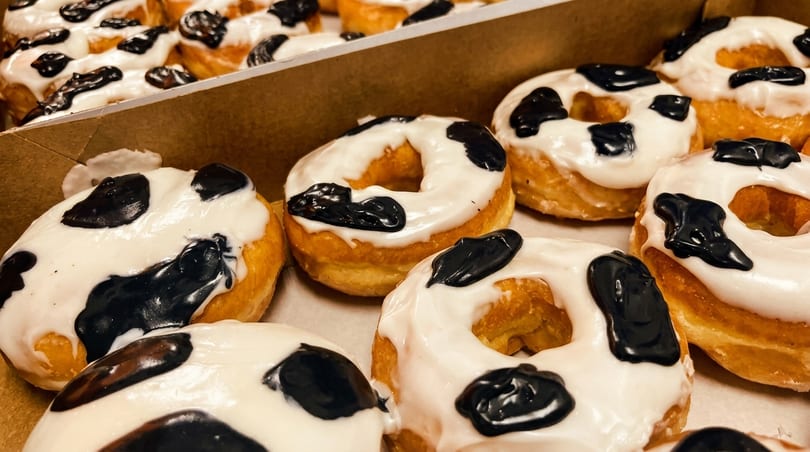 A box filled with many cow-print donuts, featuring white glaze with black splotches.