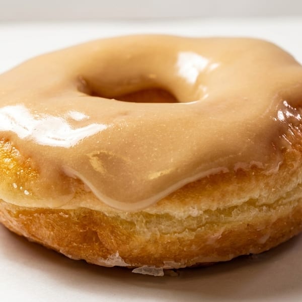 A single glazed donut with a light brown, shiny frosting on a white background.