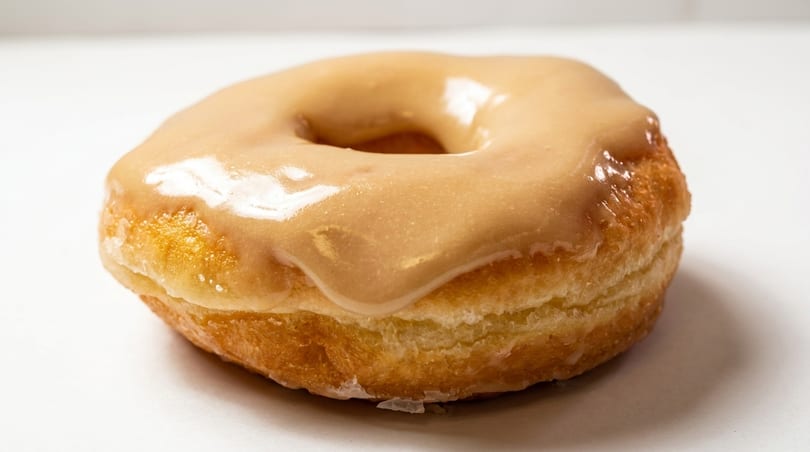 A single glazed donut with a light brown, shiny frosting on a white background.