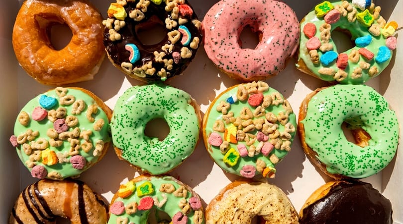 A dozen colorful donuts with various frostings and toppings, including cereal and sprinkles.